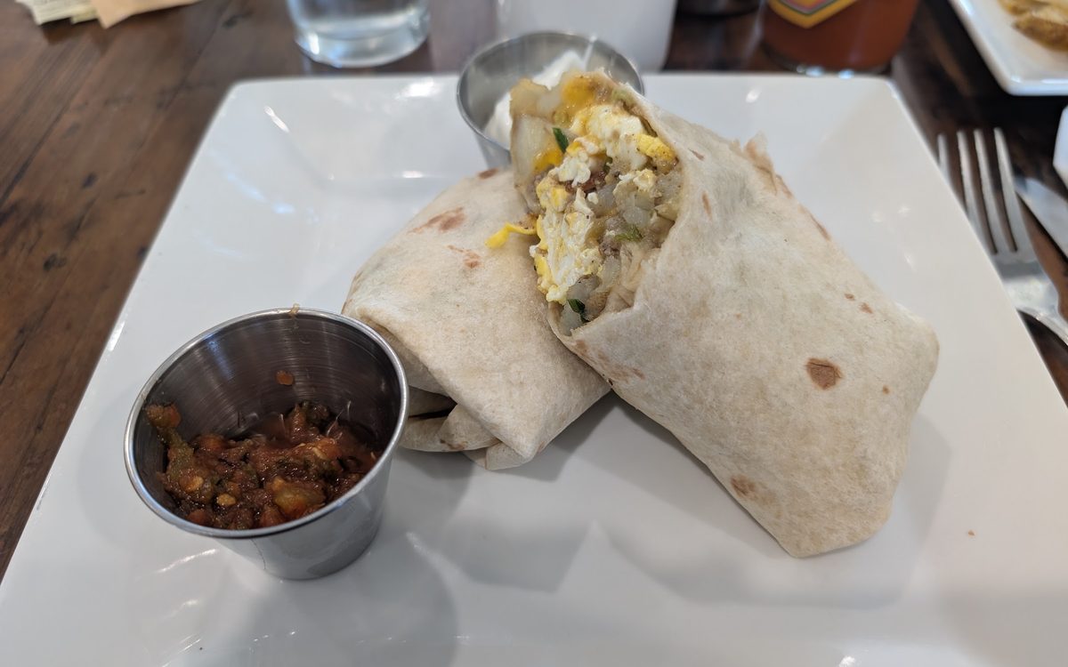 A breakfast burrito cut in half on a white plate with a cup of salsa