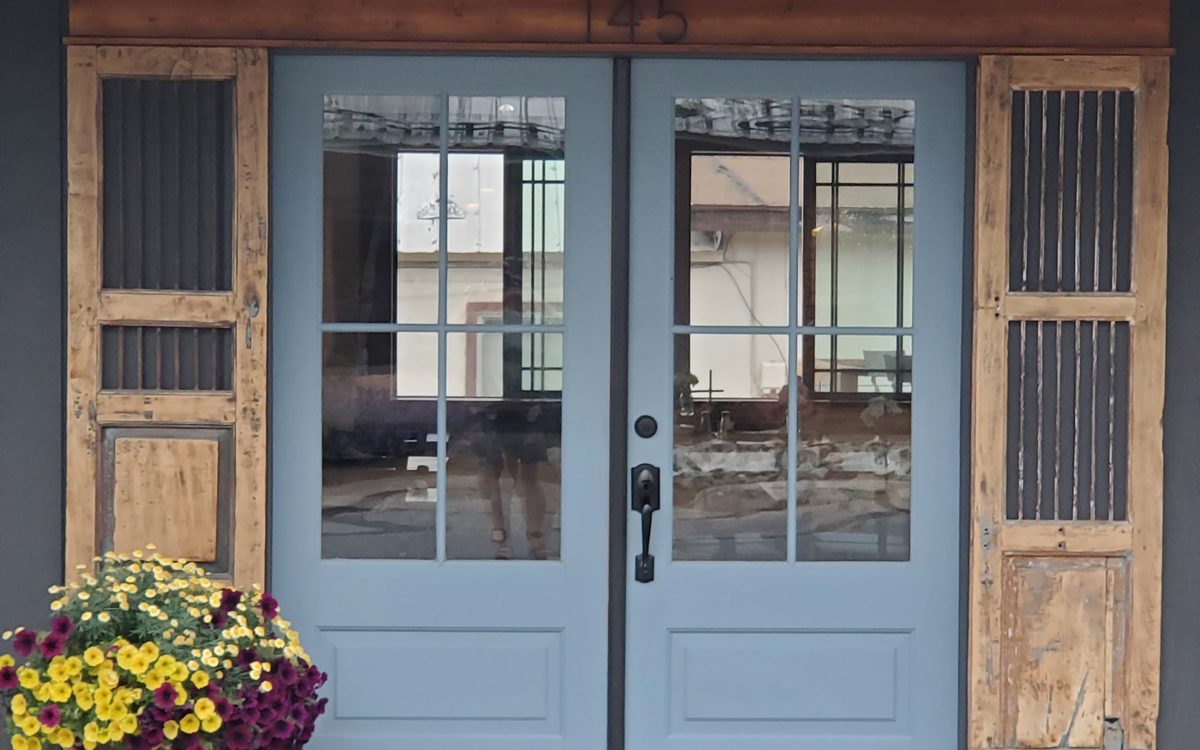The powder-blue double front door of Blue Door Cafe with chrysanthemums in bloom beside the step